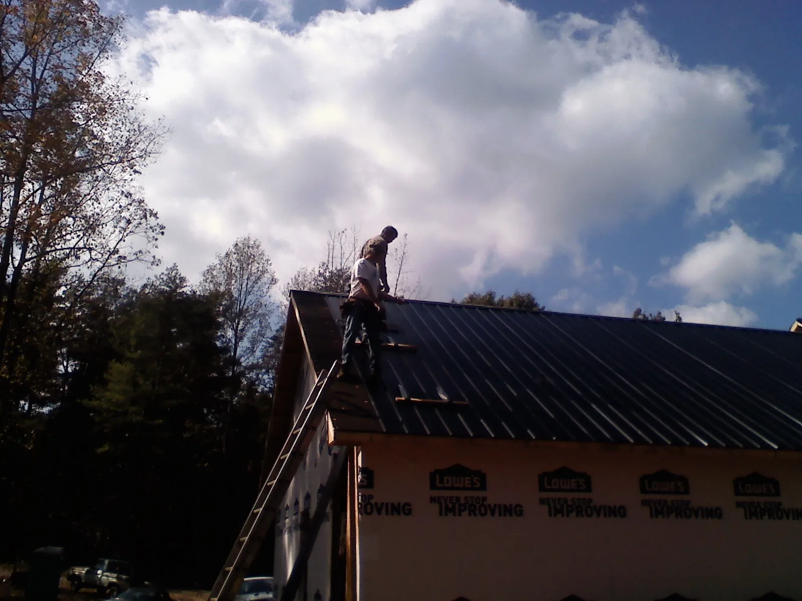 Roofer fastening dark metal panels high against a cloudy sky, from a Roof Inspection job in Martinsburg